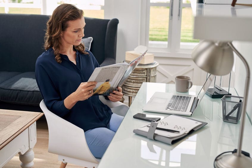 woman reading business magazine at home office desk woman reading business magazine at home office desk